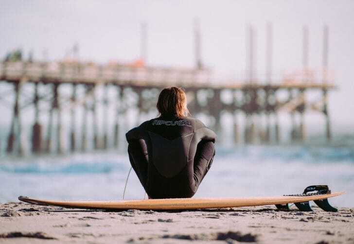 海辺でサーフボードに腰掛ける男性の写真