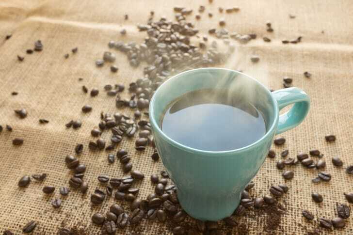 コーヒーが入ったカップと周りに散らばる豆の写真