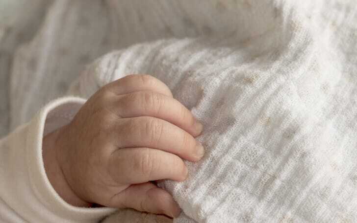 白いガーゼの布を赤ちゃんの手がつかんでいる画像