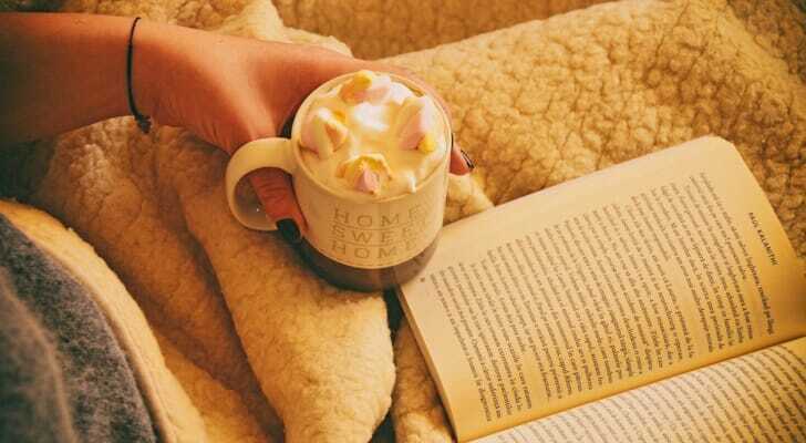 ブランケットに包まれ、本を読みながらホットチョコレートを飲む姿