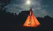 夜のキャンプ場に光るワンポールテントの写真