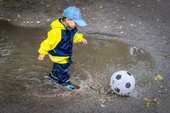 レインコートを着てサッカーをする子供の画像
