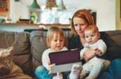 two babies and woman sitting on sofa while holding baby and watching on tablet