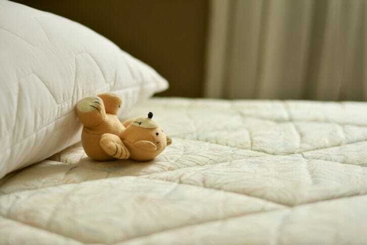 白いベッドにクマのぬいぐるみが置いてある写真