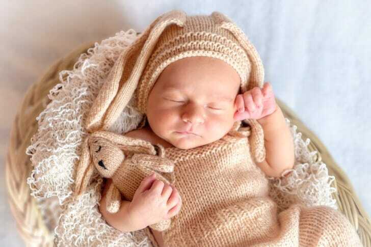 うさぎのような服を着せられ、うさぎのぬいぐるみをだっこしたまま寝ている赤ちゃんの写真