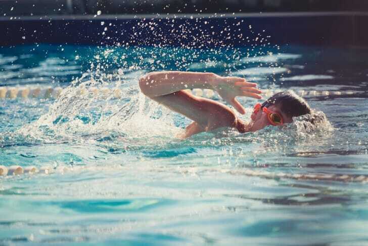 ゴーグルをつけた子供がプールで泳いでいる写真