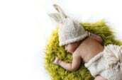 baby in white knit cap lying on green fur textile