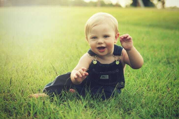 草原の中、笑顔の赤ちゃんがこちらを向いて座っている写真
