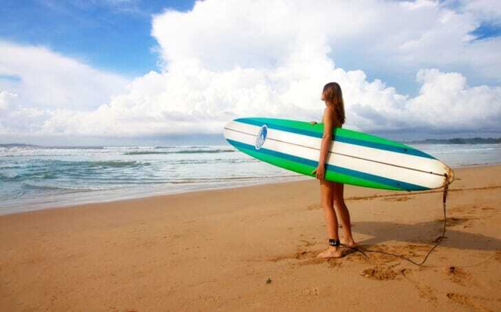 砂浜で女性がサーフボードを抱えている画像