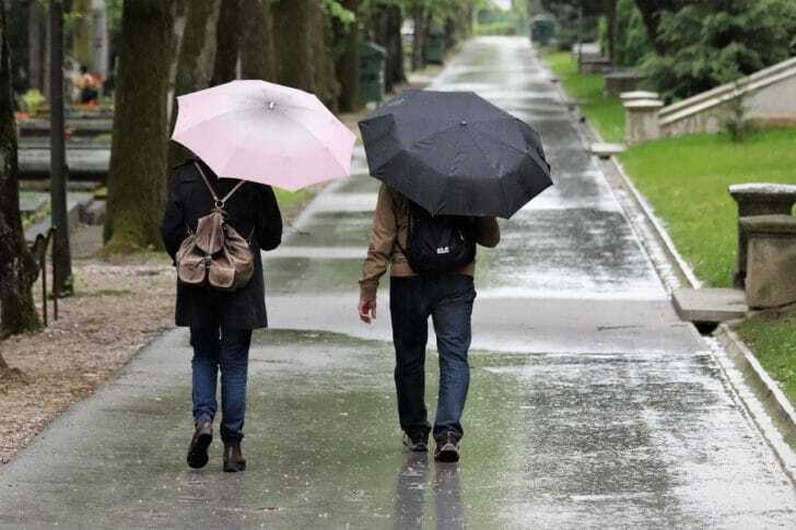 折りたたみ傘を差して歩く男女の画像