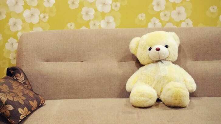 浅めのソファにぬいぐるみのクマが添えられている写真