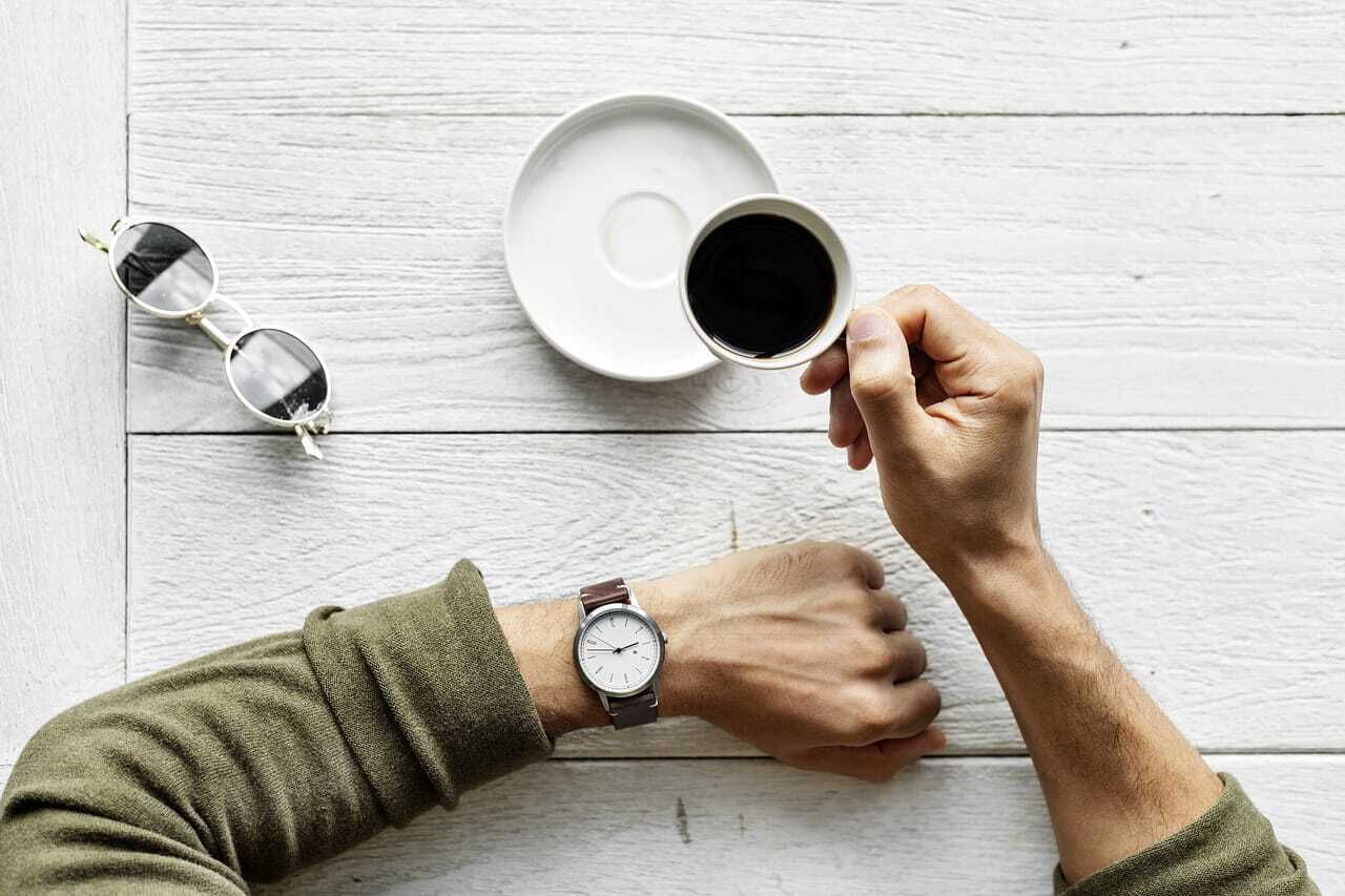 男性がコーヒーを飲みながら腕時計を見ている写真